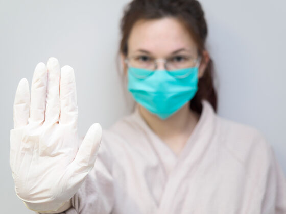 改善一位戴着橡胶手套和防护面具的欧洲年轻女子伸出手来做了个停车手势美女感染病人