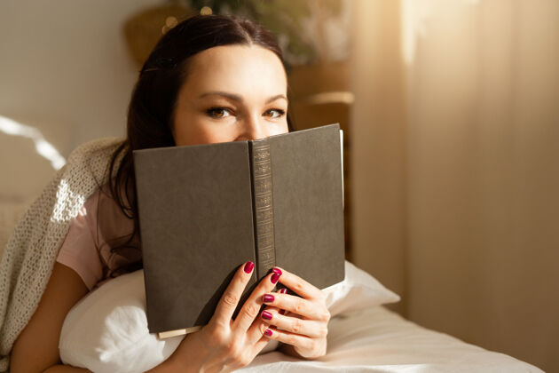 积极漂亮的年轻女子在卧室的床上拿着一本书肖像微笑女人