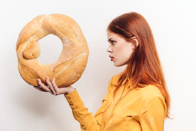 表情一个女人手里拿着一个圆面包 站在一堵浅色的墙上 一件黄色衬衫被剪成了短形女性面包室内