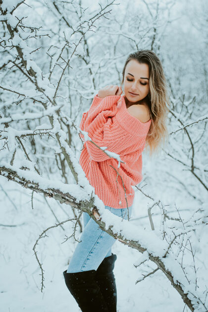 性感一个穿着粉色宽松毛衣和牛仔裤的漂亮女孩在寒冷的雪域森林里快乐微笑公园