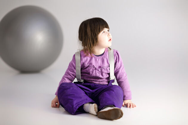 紫色穿着紫色衣服的可爱小女孩 灰色背景上有一个健身用的大球运动欢笑跳跃