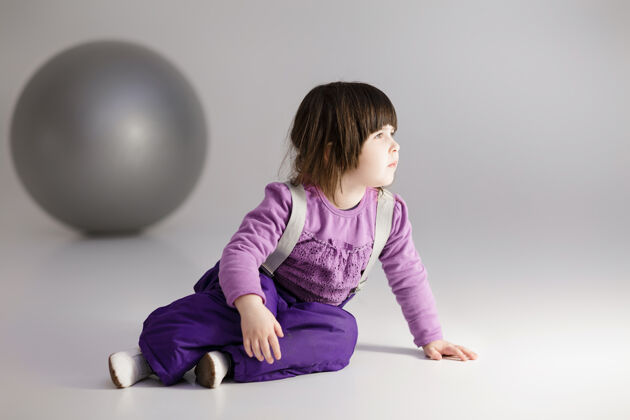 背景穿着紫色衣服的可爱小女孩 灰色背景上有一个健身用的大球精力充沛跳跃孩子