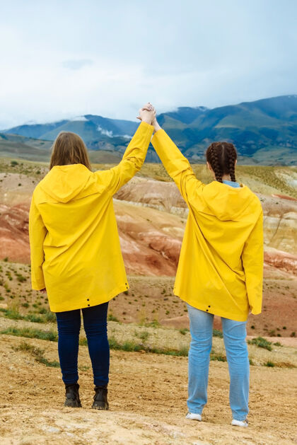 女性两个女人手牵着手走在彩色山脉的背景上友谊旅行者户外