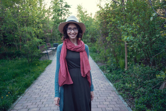 肖像一个美丽的怀孕的年轻女子喜欢在一个美丽的绿色公园散步帽子公共怀孕