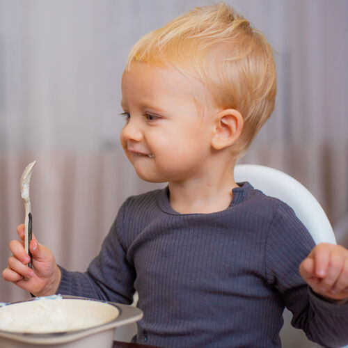 零食可爱的蹒跚学步的孩子拿着勺子在桌边吃早餐菜单幼儿男性