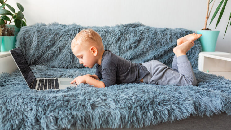 距离小男婴躺在沙发上玩笔记本电脑电子学习 远程学习 远程交流的概念聊天流你好