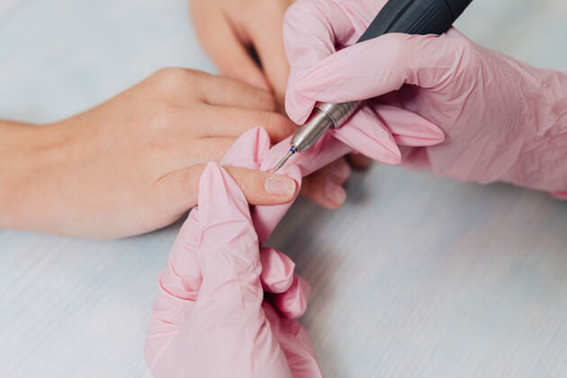 仪器修指甲的过程一位戴着粉色橡胶手套的用电动指甲打磨指甲文件.female把手收起来橡胶美容师美甲师