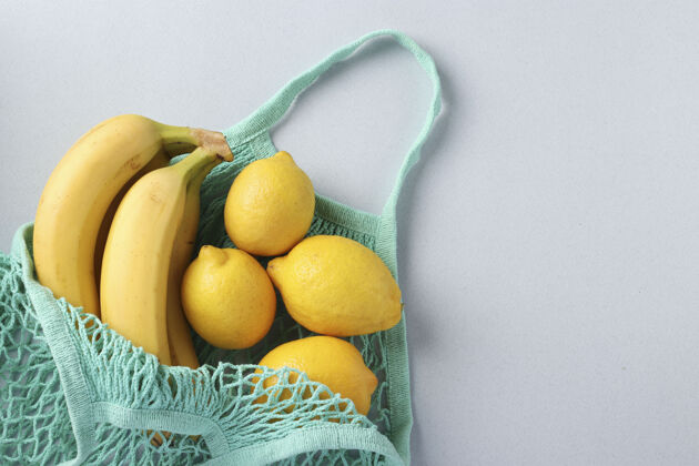 热带黄色成熟的香蕉和柠檬在绿松石线网袋轻表面 零浪费的概念 文字空间水果字符串袋零浪费