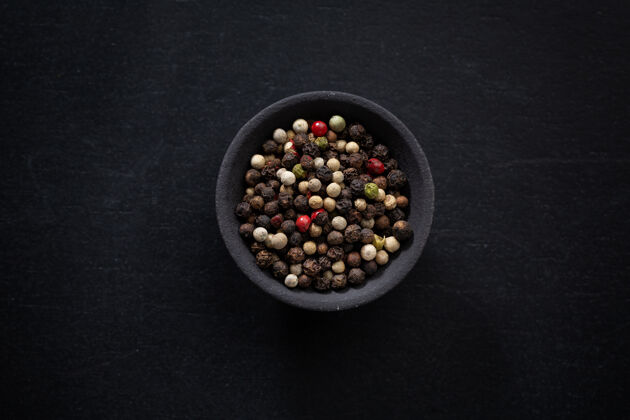 香草把整个胡椒粉放在一个小碗里 在深色的背景上涂上颜色圆形香料特写