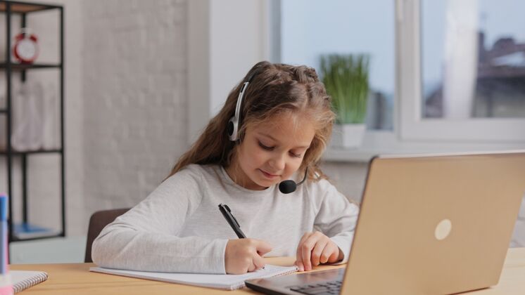 留在家里女生在耳机里有在线课 视频通话用老师可爱小学女生在家用笔记本电脑学习远程教育数字学生