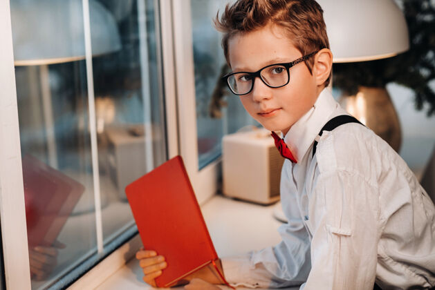 小商人窗口站着一个男孩 穿着衬衫 打着红色领结 戴着眼镜 手里拿着一本红色的书Wifi室内笔记本
