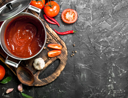 蔬菜番茄酱放在菜板上的锅里 上面放着大蒜和番茄片配料西红柿营养