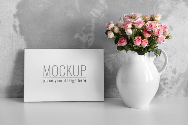 艺术家白色桌子上的空白帆布模型 水泥墙背景上的花瓶里有粉色的花灰色混凝土花瓶