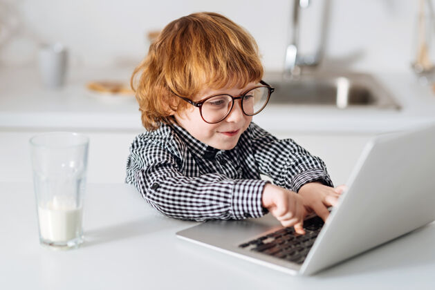 学习探索好主意有趣聪明的红发男孩戴着眼镜坐在阳光明媚的厨房里的桌子旁 用笔记本电脑打字测试房子课堂论文