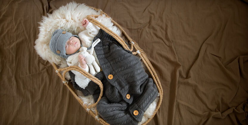 新生儿婴儿在柳条摇篮里睡得很香 在温暖的毛毯下戴着一顶温暖的针织帽子 把手上放着一个玩具顶视图睡眠格子