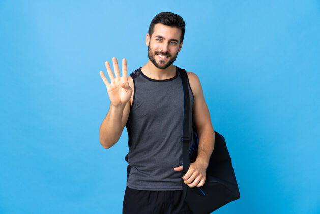 计数拿着运动包的年轻人在蓝色的沙滩上快乐地数着四个手指想法健身房包
