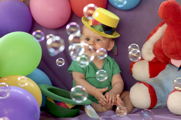 坐男孩坐在一个有趣的节日气氛与气球和看肥皂泡帽子配件气球