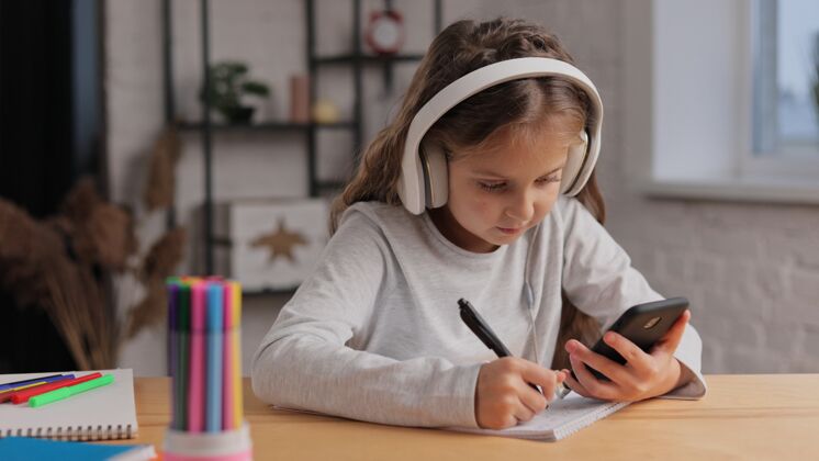 耳机戴着耳机在家学习的可爱女孩我是女学生有网络课 写练习本 做作业耳机小学生移动