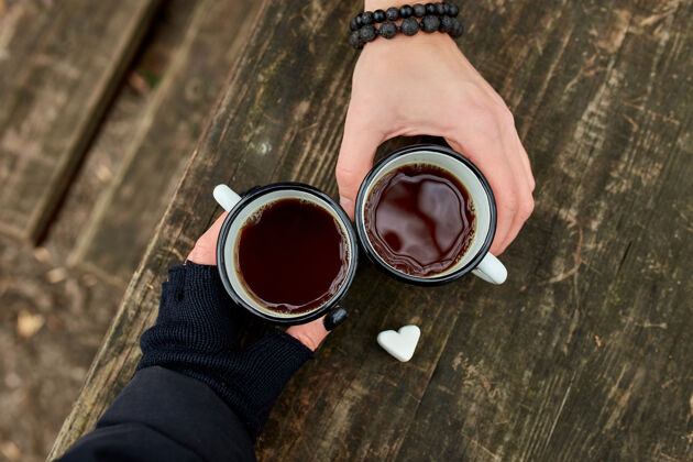 炎热两杯茶在大自然中的情侣手中 戴着黑手套放在木头表面家庭形状休闲