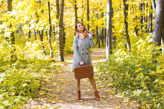 女孩人 季节 自然理念——年轻女子提着行李箱在秋园漫步人年轻秋天