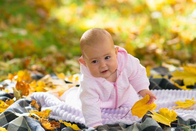 玩耍在一个明亮的秋天公园里 一个婴儿在秋叶间的野餐地毯上学习爬行分散信任可爱