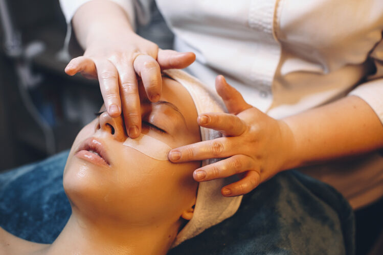 肖像美容师用手在疗养胜地的女性脸上敷上抗衰老面膜人皮肤护理专业