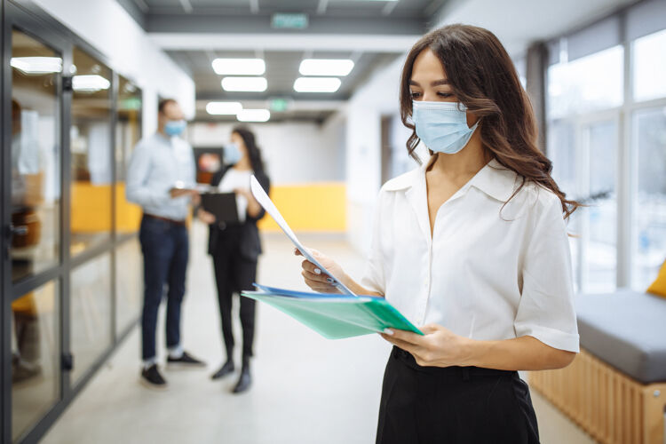 病毒一个年轻的女商人戴着医用口罩 在办公室走廊里查看报纸和商业趋势和前景的画像团队疾病笔记本电脑