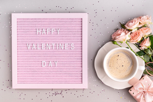板在咖啡杯和鲜花旁边的粉色毡纸上写着“情人节快乐”字样礼物形状浪漫
