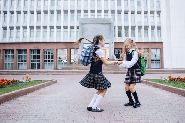 小学生两个穿着校服的女学生站在一起 在学校门前拥抱着男性小学生微笑
