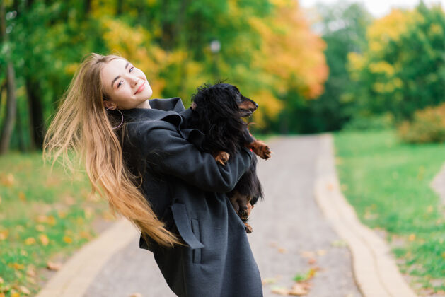 友谊秋天公园里日出时分 一位年轻迷人的女士抱着她的腊肠狗在户外腊肠腊肠小狗纯种