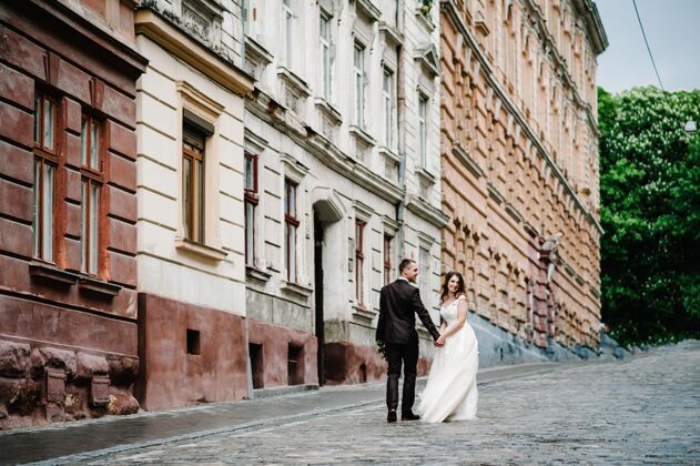 爱情描绘新郎和新娘回到老房子附近 外面的老房子 户外新婚夫妇走在利沃夫市的街道上姿势西装街道