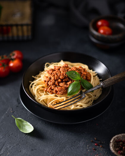 传统意大利肉酱意大利面放在一个黑碗里 桌上放着樱桃番茄盘子罗勒菜肴