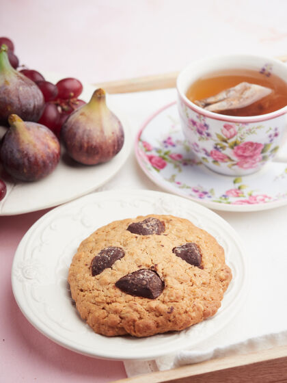 饼干燕麦片饼干和巧克力片旁边的一杯茶装饰着鲜花和新鲜水果的盘子烘焙美味水果
