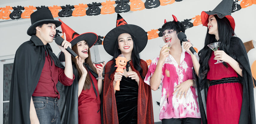叮当一群年轻的亚洲人穿着女巫的服装 和巫师一起欢庆万圣节派对 为他们唱歌喝酒 吃甜点房间.组泰语青少年万圣节概念在家里过万圣节十月歌手亚洲