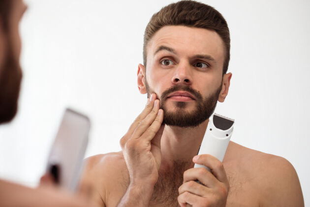 肌肉英俊的年轻人在街上刮胡子浴室.肖像一个时髦的裸体胡须男人在家里的镜子里检查他的脸房子治疗早晨