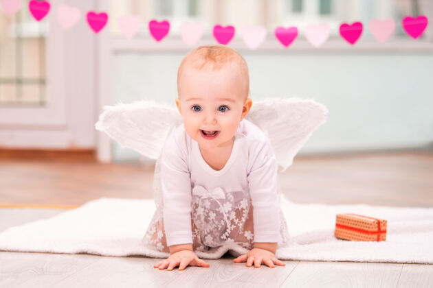 幼儿一个快乐淘气的婴儿的肖像 白色天使翅膀爬向观众光明心微笑