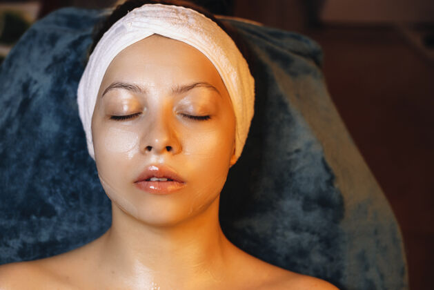 美容师俯视图：一位可爱的女士靠在水疗床上 闭着眼睛 戴着透明质酸面膜放松专业放松自由空间