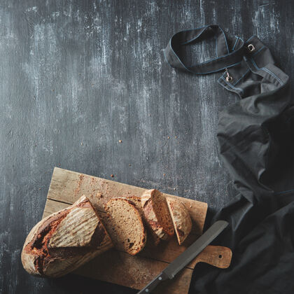 圆形烘焙和烹饪概念背景.切片黑暗面包面包把刀放在深色背景的木板上静止木板美食