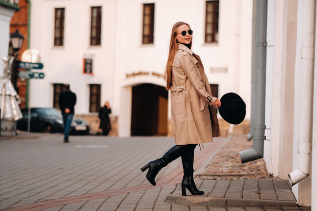 脸一个穿着米色外套 戴着黑帽子 戴着眼镜的时髦年轻女子街头女人的街道时尚.秋季服装.城市风格城市春装衣服