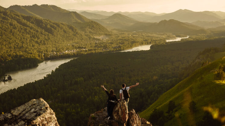 夫妇背影：一对背着背包的游客 一男一女举起手在山顶上度假旅行和冒险的概念年轻风景赢家
