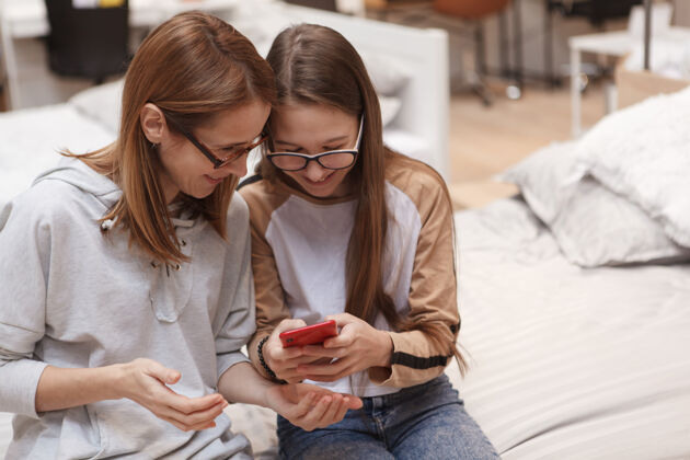 青少年十几岁的吉尔在给她妈妈看她的智能手机设备连接零售