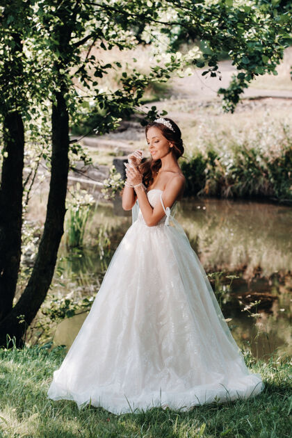 肖像一个优雅的新娘穿着白色礼服 戴着手套和花束在公园的瀑布上欧洲立场新娘