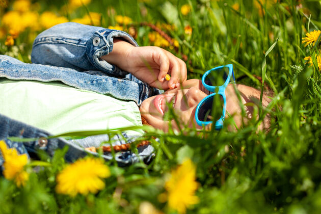 可爱夏天 戴墨镜的时髦女婴躺在公园的草地上草阳光玩