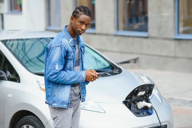 车辆男人在等待时使用智能手机 电源连接到电动车上为车内的电池充电社交媒体燃油加油