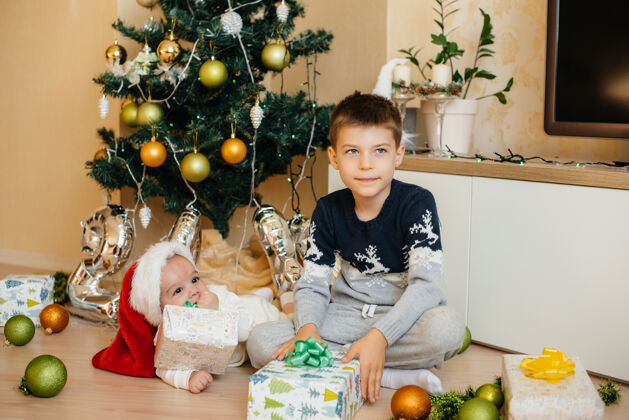 坐着一个小男孩和他的弟弟在圣诞树下玩礼物年房子玩