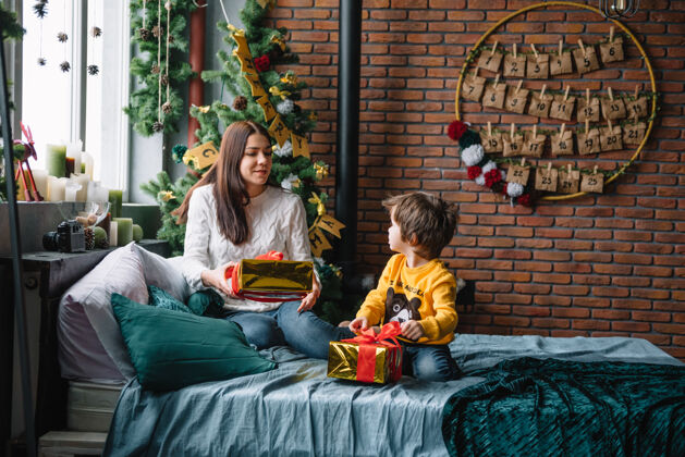 盒子年轻美丽的母亲带着可爱的儿子在圣诞树旁礼物快乐圣诞节阁楼孩子微笑