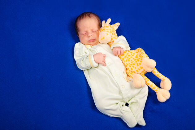 睡衣可爱的新生婴儿躺在蓝色的毯子上和玩具长颈鹿健康睡眠怀孕