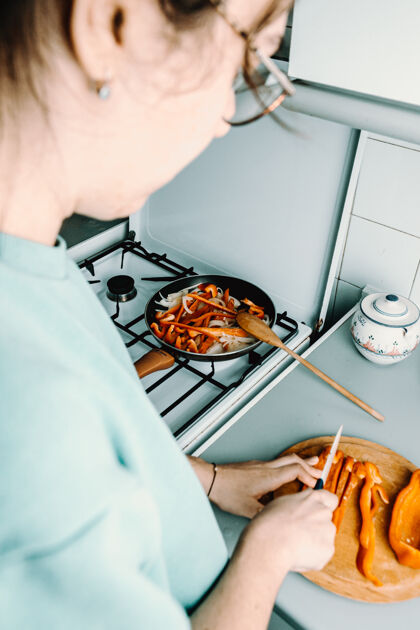 炉子一个女人在厨房里用锅做饭时 用刀在木制圆板上切胡椒脸女人芦笋