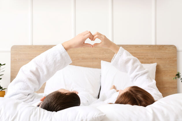 懒惰躺在床上用手做心形的年轻夫妇男性使心
