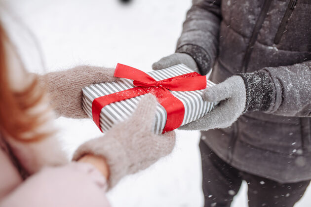 欢呼在下雪的冬天 一对恩爱的夫妇戴着羊毛手套在外面互相送礼物公园条纹一个男人手里拿着红色蝴蝶结的盒子瓦伦丁女士情人节概念女人情人节爱情人节外面